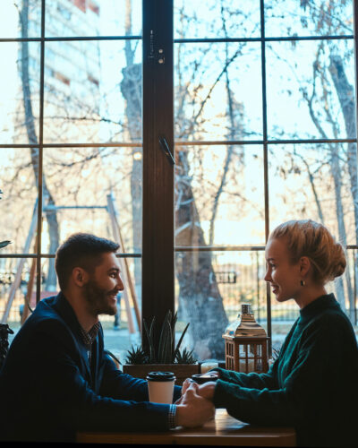 Romantic couple is sitting at cafe at their date Happy smiling couple of attractive people sitting and cafe and warming up with coffee.